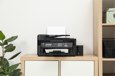 Photo of Modern printer with paper on wooden nightstand in office