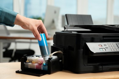 Photo of Woman refilling ink in modern printer at workplace indoors, closeup