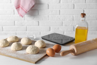 Raw dough balls, eggs, oil, rolling pin and kitchen scale on white wooden table