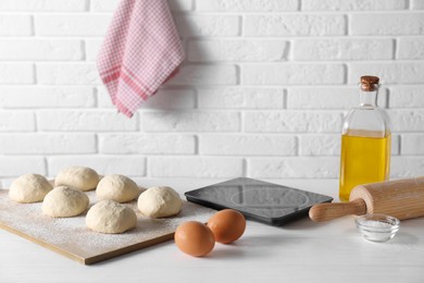 Photo of Raw dough balls, eggs, oil, rolling pin and kitchen scale on white wooden table