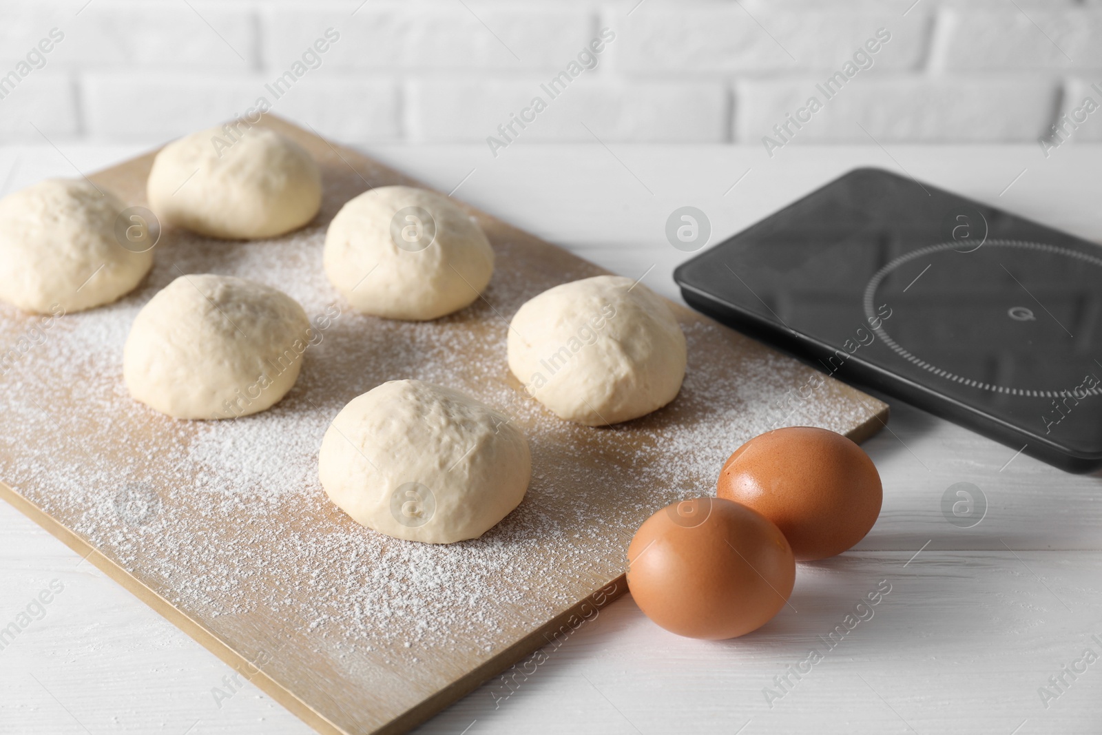 Photo of Raw dough balls, eggs and kitchen scale on white wooden table