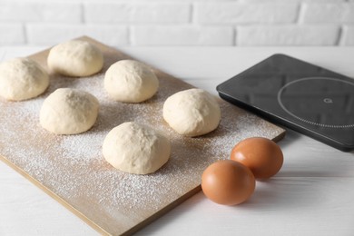 Photo of Raw dough balls, eggs and kitchen scale on white wooden table