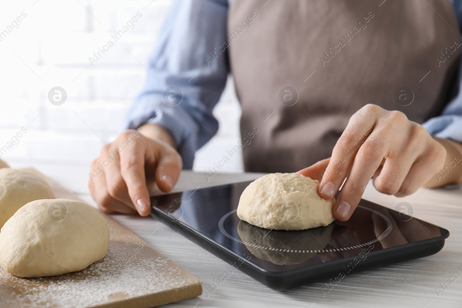 Photo of Woman weighing raw dough ball on kitchen scale at white wooden table, closeup