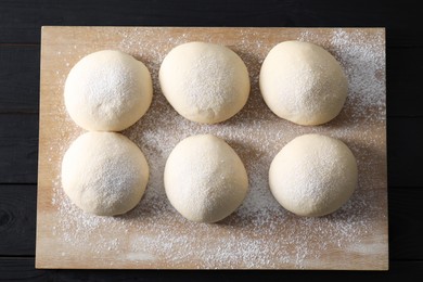 Photo of Raw dough balls on black wooden table, top view