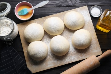 Photo of Raw dough balls, yolk, flour, salt and rolling pin on black wooden table, top view