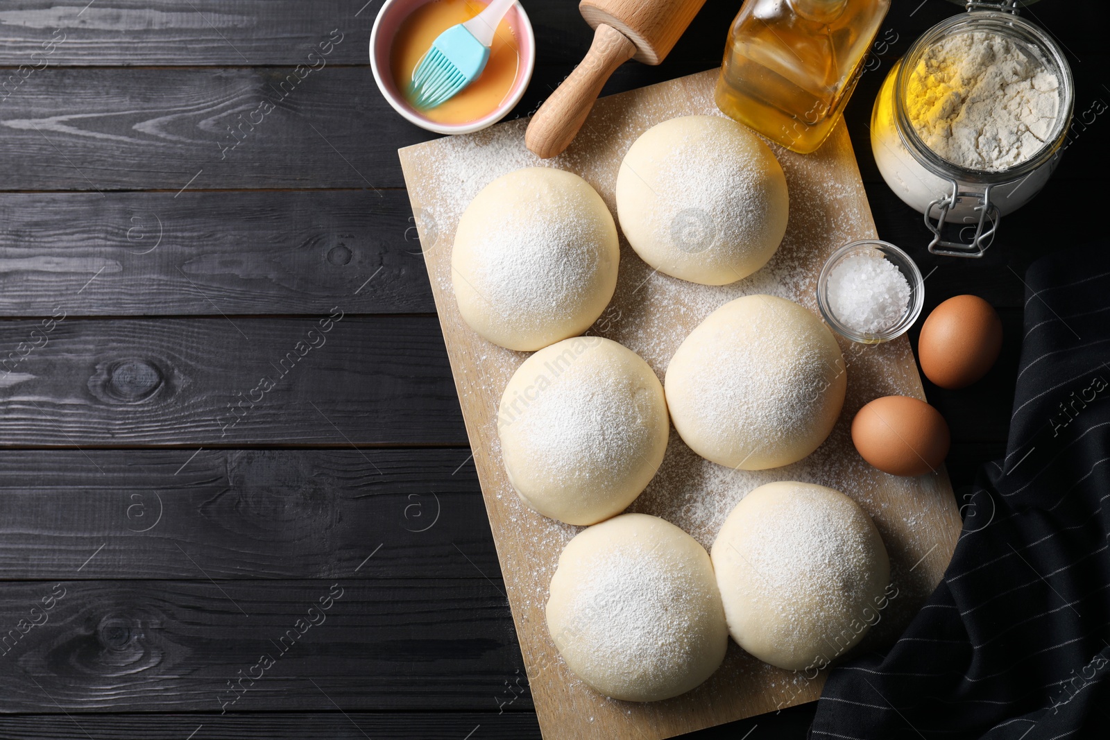 Photo of Raw dough balls, yolk, flour, eggs and rolling pin on black wooden table, top view. Space for text