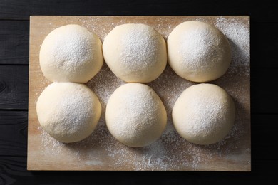 Photo of Raw dough balls on black wooden table, top view