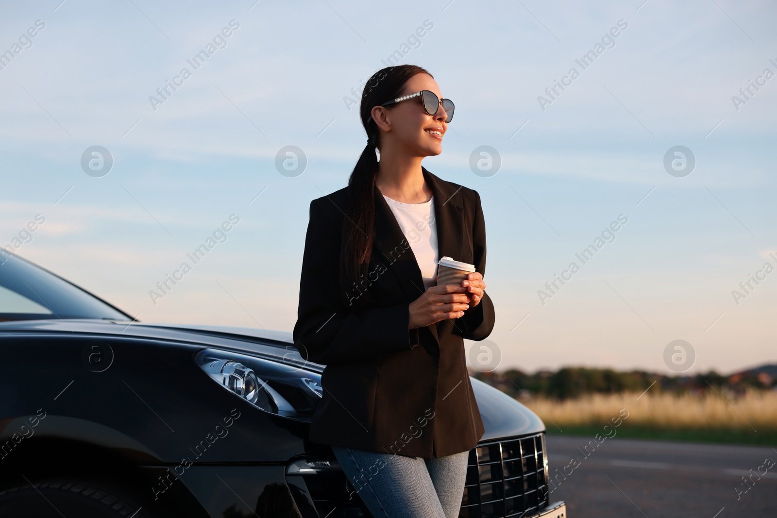 Photo of Smiling woman in sunglasses with paper cup of drink near car outdoors