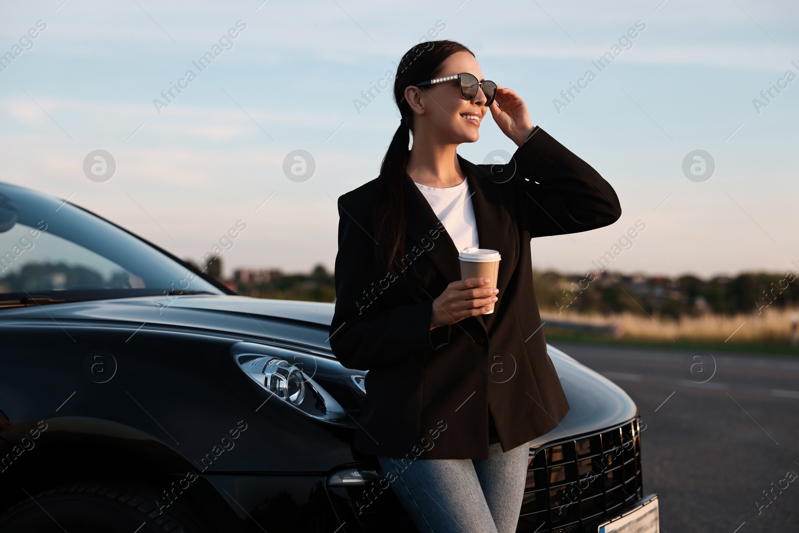 Photo of Smiling woman in sunglasses with paper cup of drink near car outdoors