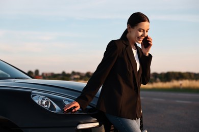 Smiling young woman talking on smartphone near car outdoors