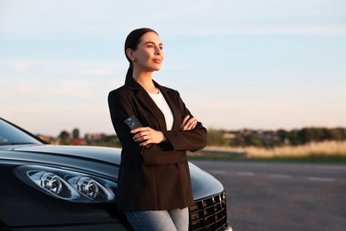 Beautiful young woman with smartphone near car outdoors