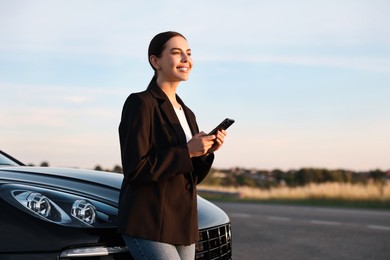 Smiling young woman with smartphone near car outdoors