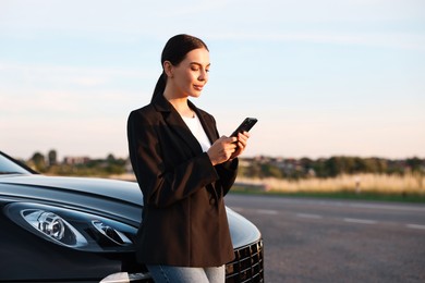 Beautiful young woman with smartphone near car outdoors