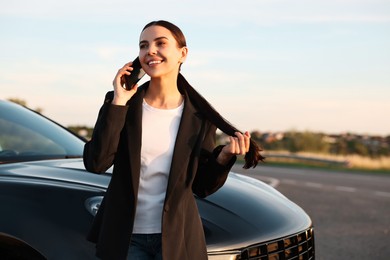 Smiling young woman talking on smartphone near car outdoors