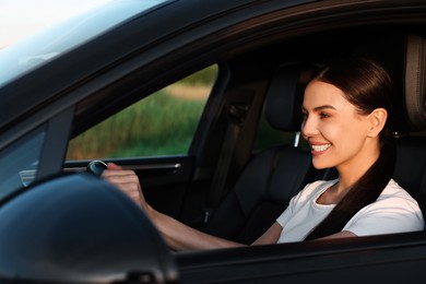 Smiling young woman holding steering wheel while driving car, view from outside