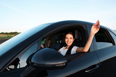 Photo of Smiling young woman holding steering wheel while driving car, view from outside