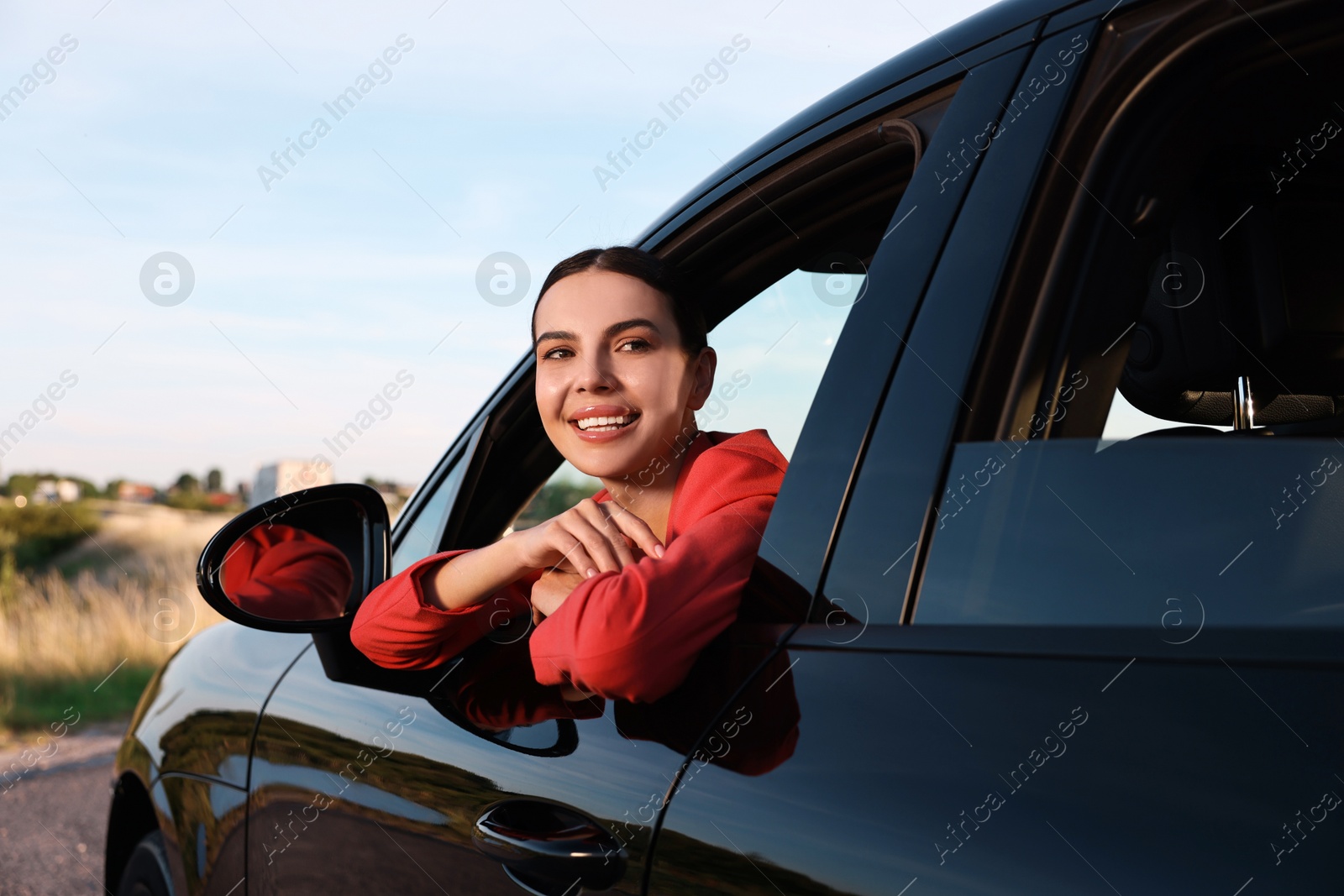 Photo of Smiling young woman leaning out of car window, view from outside. Enjoying trip