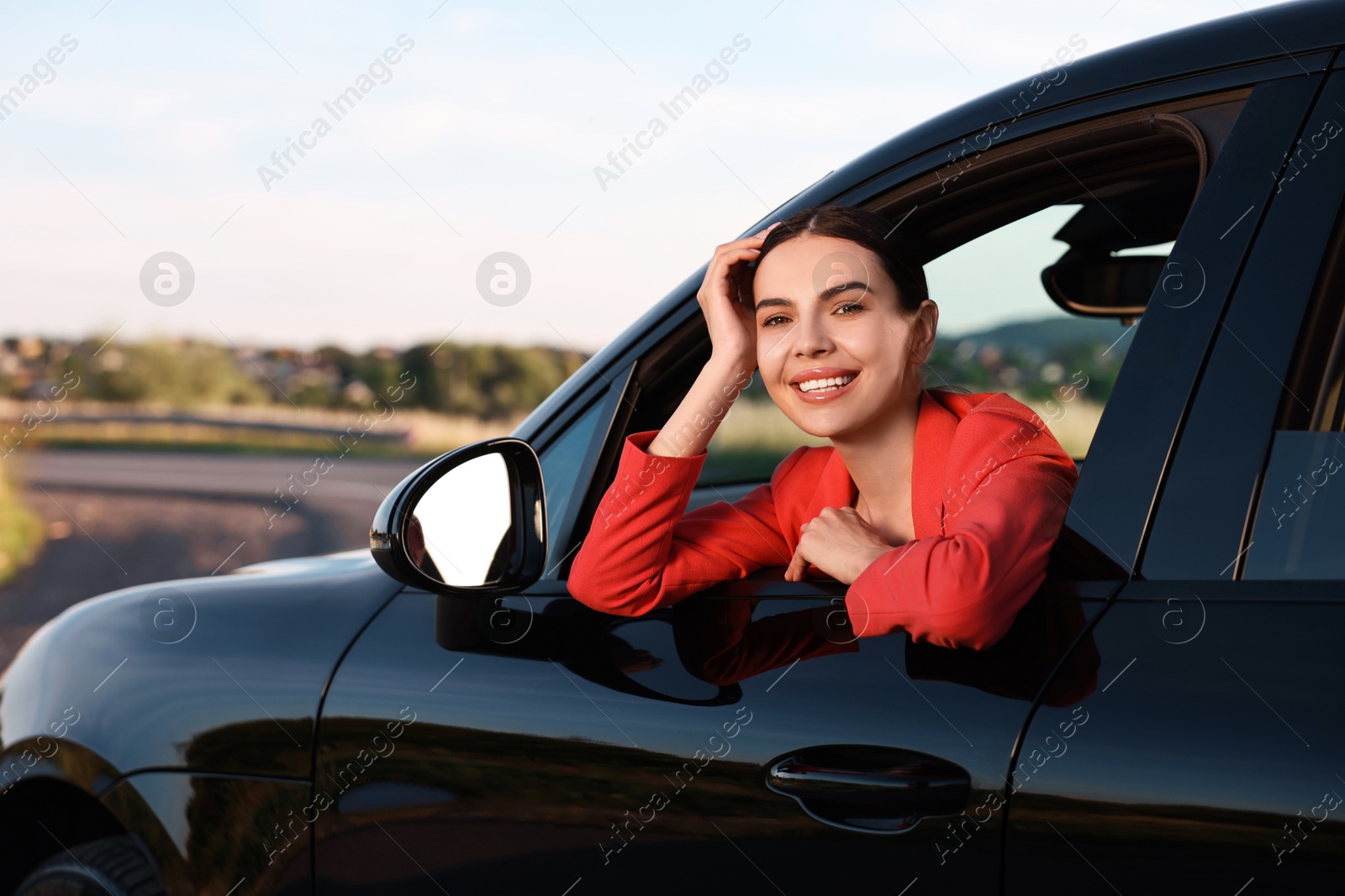 Photo of Smiling young woman leaning out of car window, view from outside. Enjoying trip