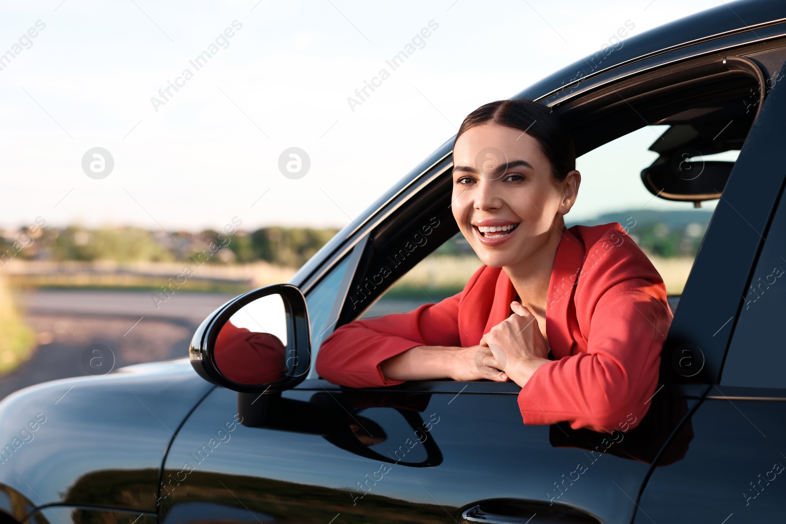 Photo of Smiling young woman leaning out of car window, view from outside. Enjoying trip