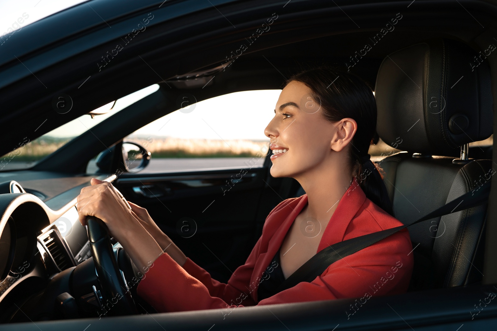 Photo of Smiling young woman with seatbelt driving car, view from outside