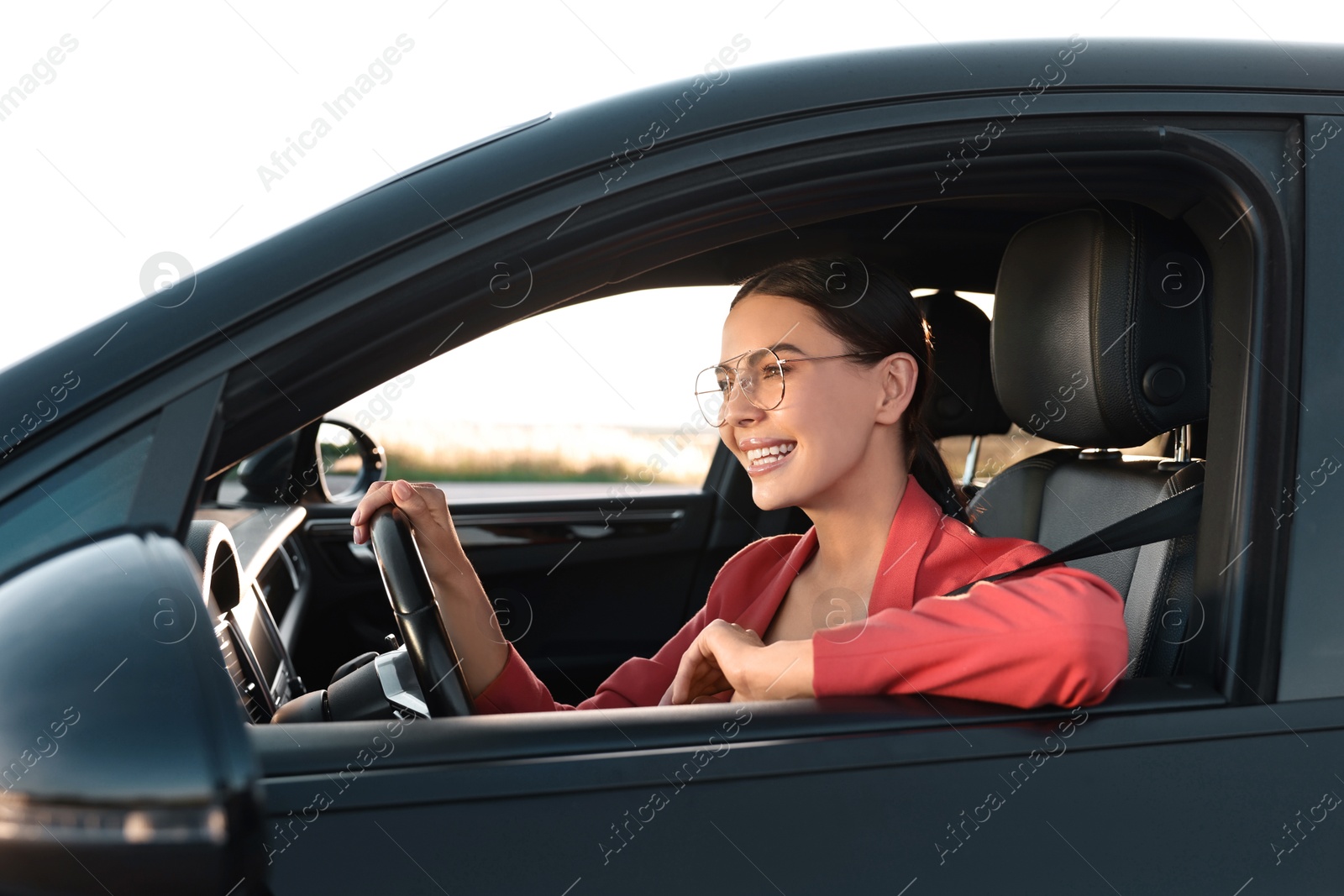 Photo of Smiling young woman with seatbelt driving car, view from outside