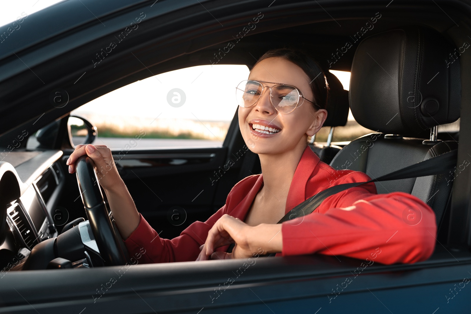 Photo of Smiling young woman with seatbelt driving car, view from outside