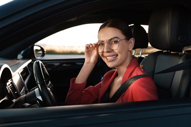 Smiling young woman with seatbelt driving car, view from outside