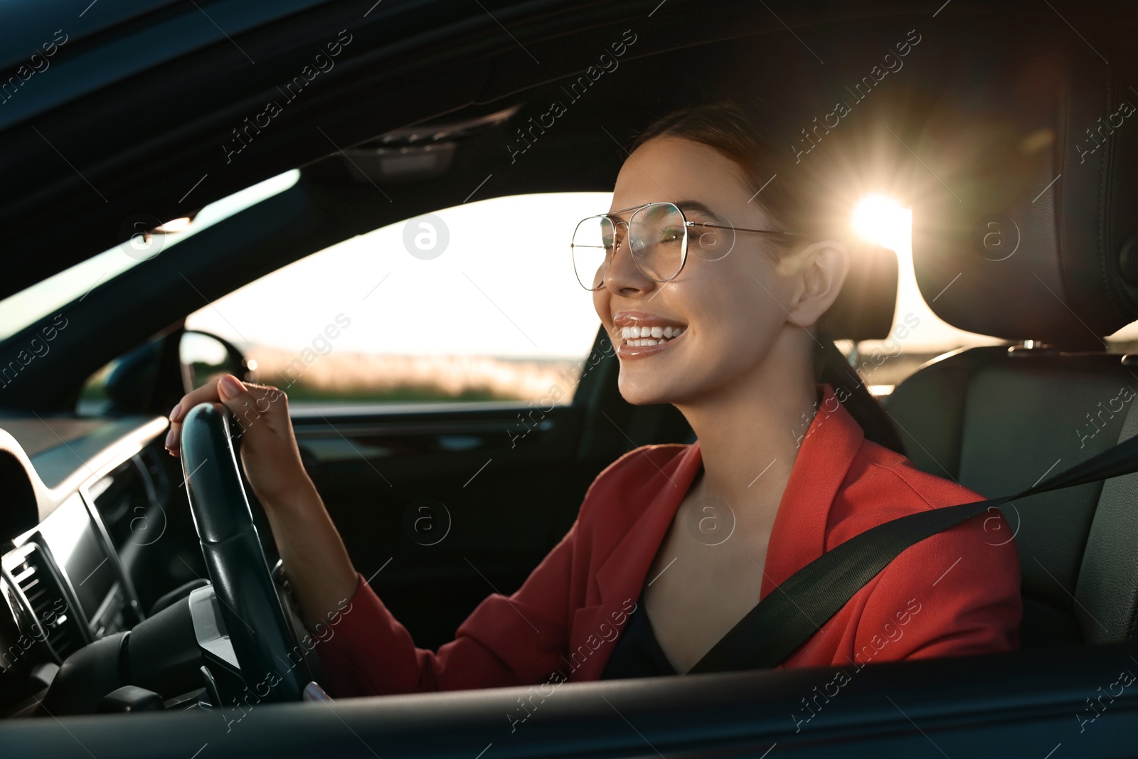 Photo of Smiling young woman with seatbelt driving car, view from outside