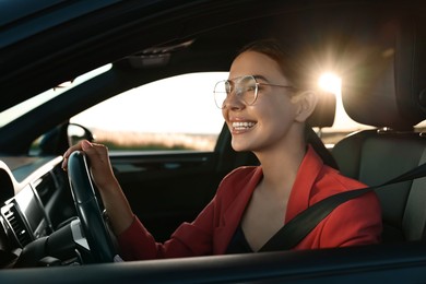 Smiling young woman with seatbelt driving car, view from outside