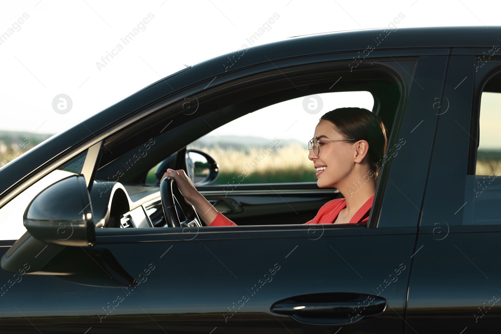 Photo of Smiling young woman with seatbelt driving car, view from outside