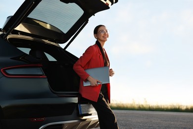 Photo of Smiling young woman with laptop near car outdoors, space for text