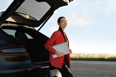 Photo of Smiling young woman with laptop near car outdoors, space for text