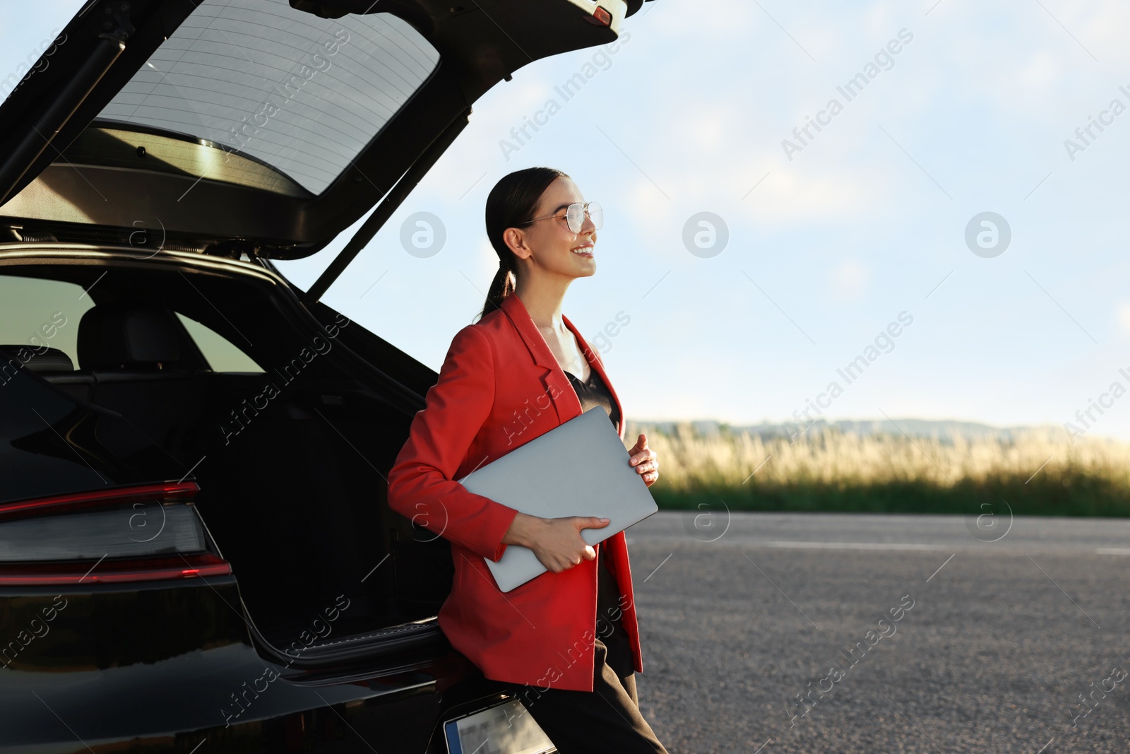 Photo of Smiling young woman with laptop near car outdoors, space for text