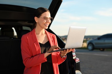 Smiling young woman using laptop near car outdoors