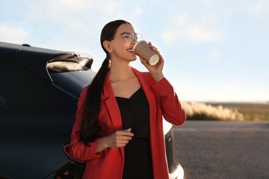 Photo of Beautiful young woman drinking from paper cup near car outdoors