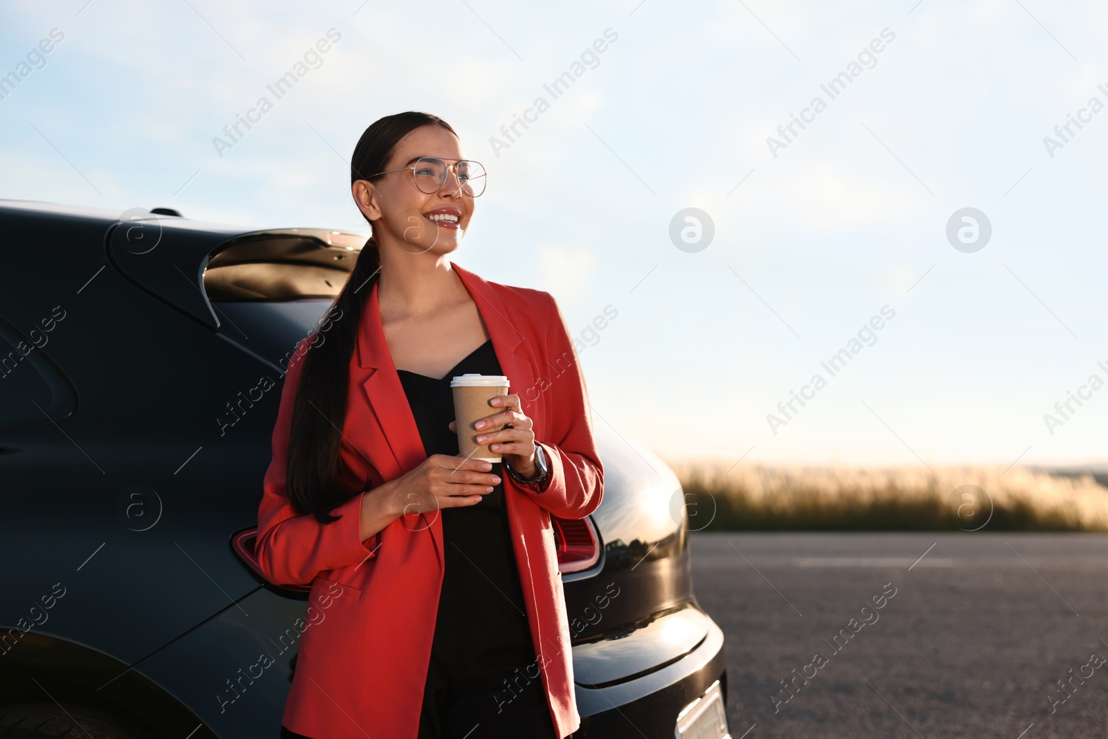 Photo of Smiling young woman with paper cup of drink near car outdoors, space for text