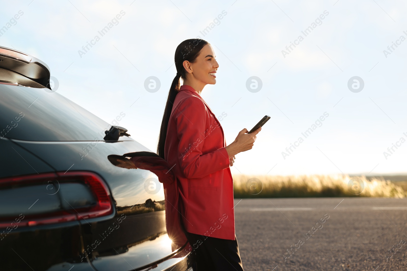 Photo of Smiling young woman with smartphone near car outdoors, space for text