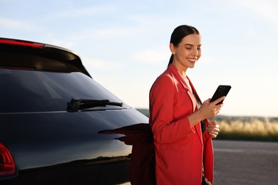 Photo of Smiling young woman with smartphone near car outdoors