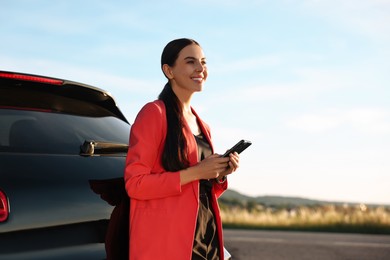 Photo of Smiling young woman with smartphone near car outdoors, space for text