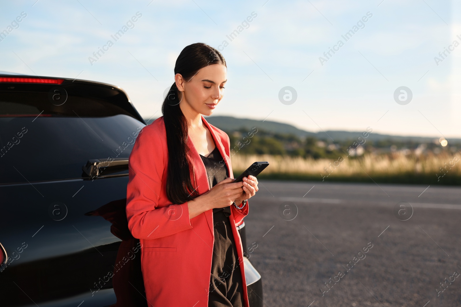 Photo of Beautiful young woman with smartphone near car outdoors, space for text