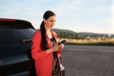 Photo of Beautiful young woman with smartphone near car outdoors, space for text