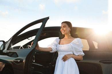 Photo of Smiling young woman near car at sunset