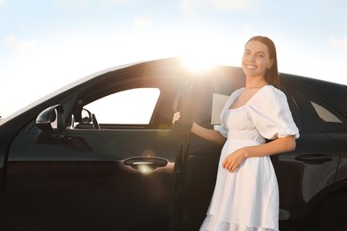 Smiling young woman near car at sunset