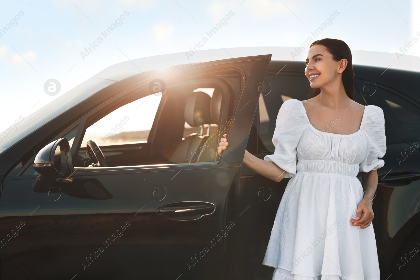 Photo of Smiling young woman near car at sunset