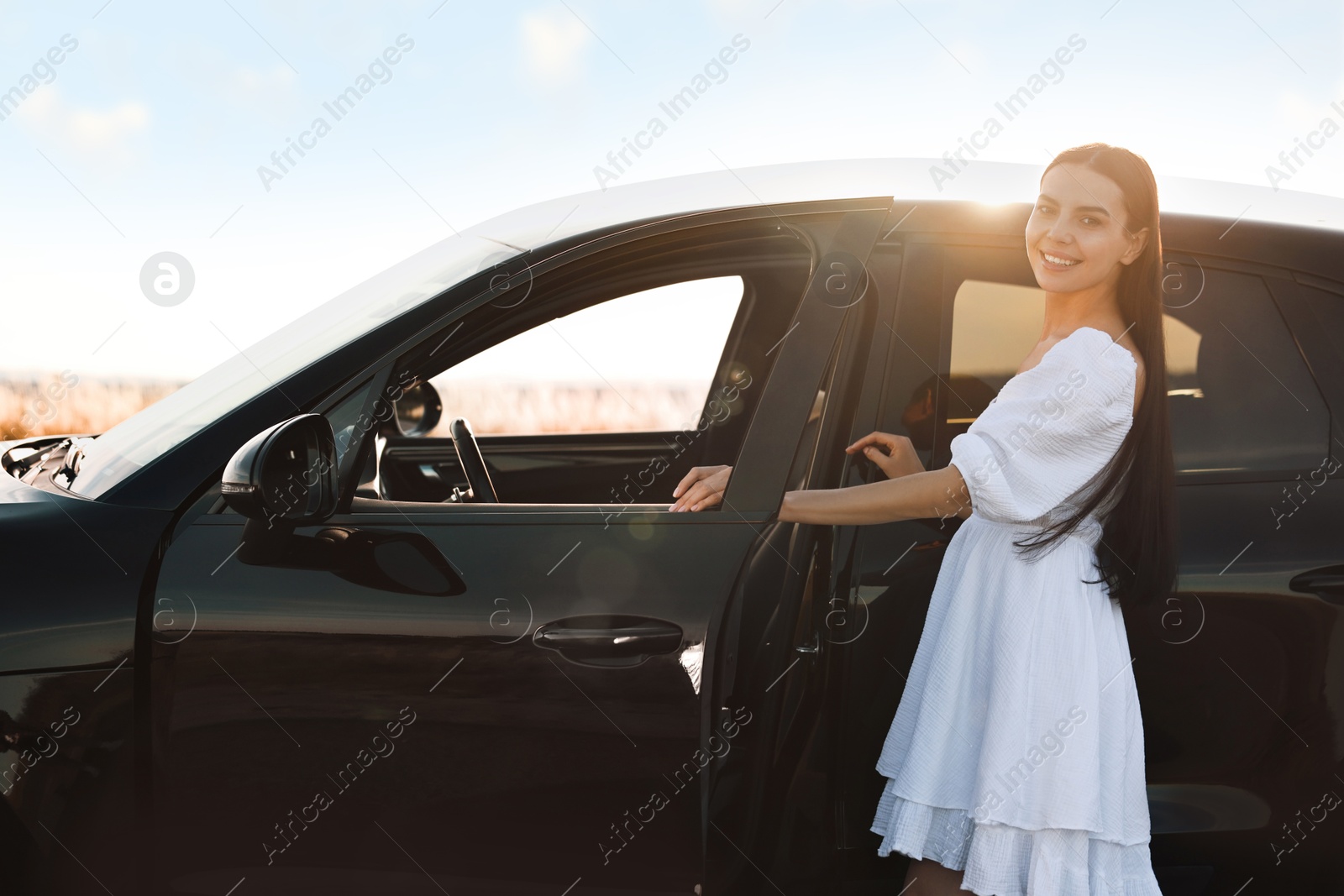 Photo of Smiling young woman near car at sunset