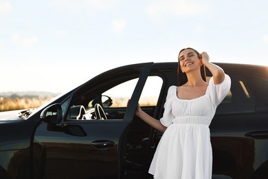 Smiling young woman near car at sunset