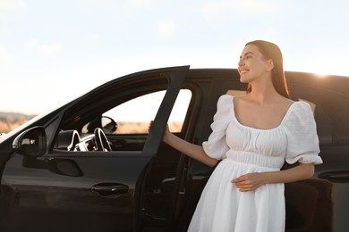 Smiling young woman near car at sunset