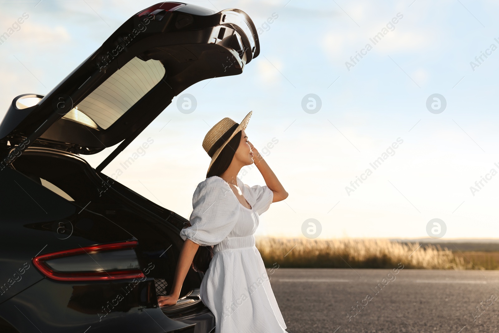 Photo of Woman in hat near trunk of car at sunset, space for text