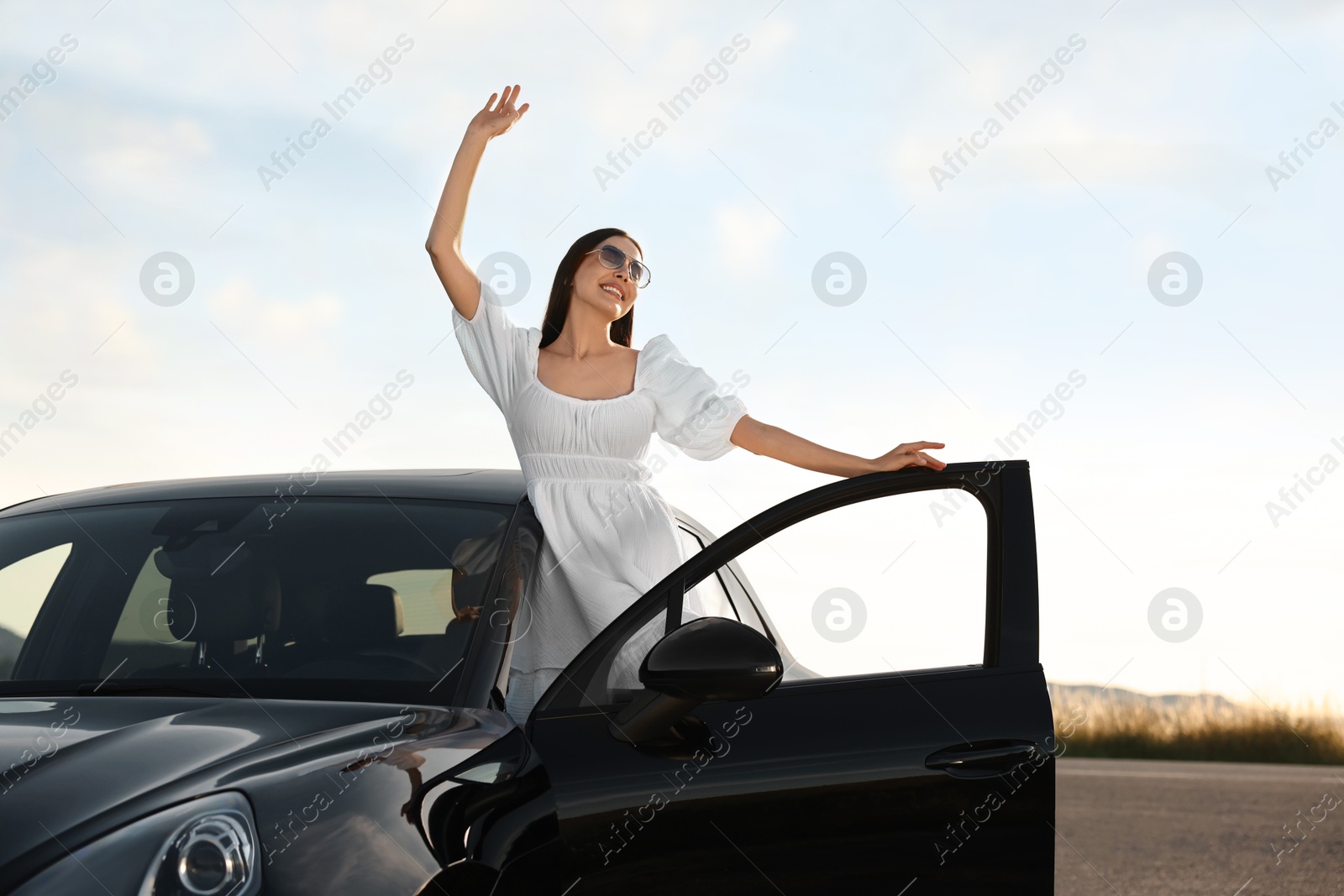 Photo of Smiling young woman in sunglasses leaning out of car outdoors. Enjoying trip