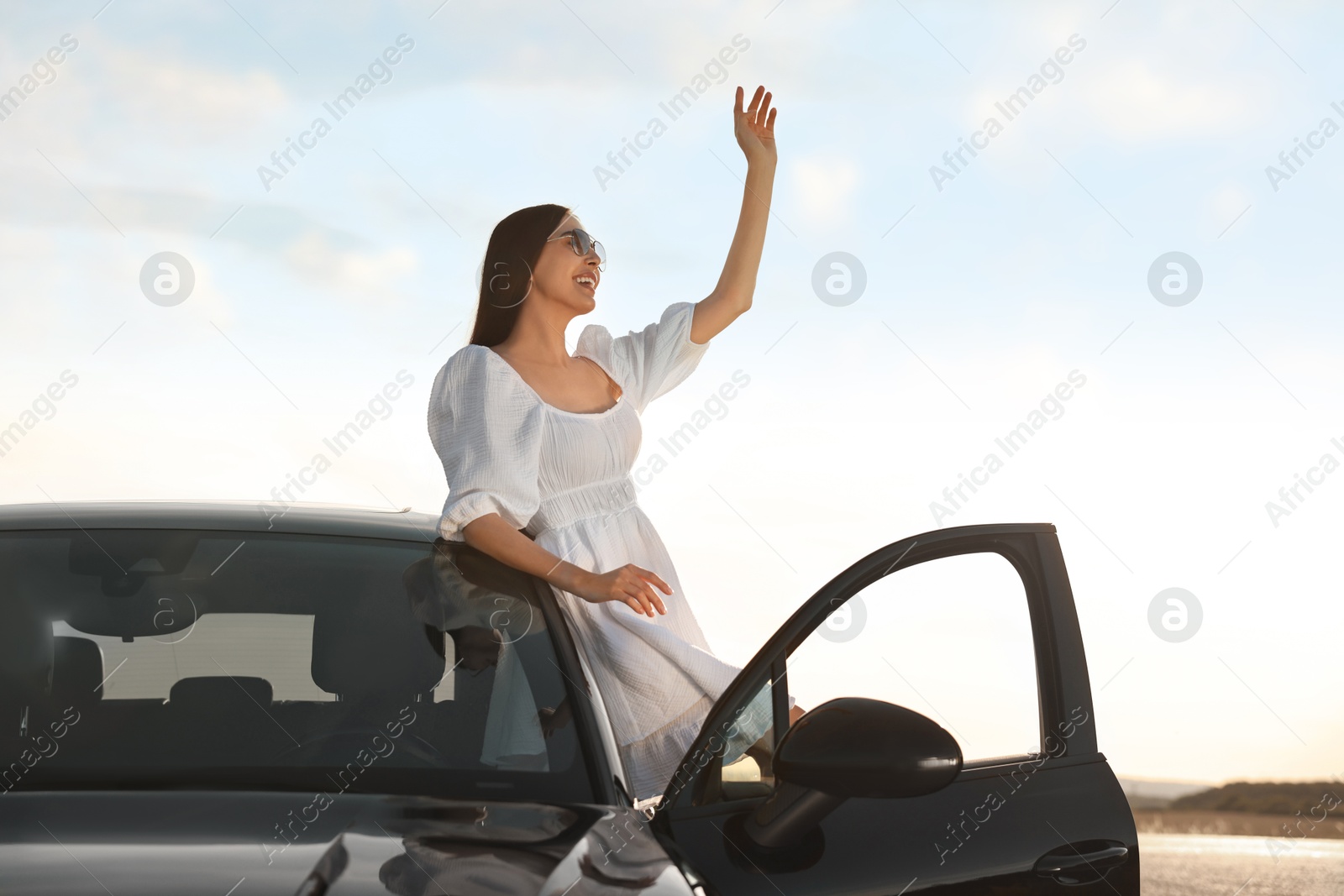 Photo of Smiling young woman in sunglasses leaning out of car outdoors. Enjoying trip